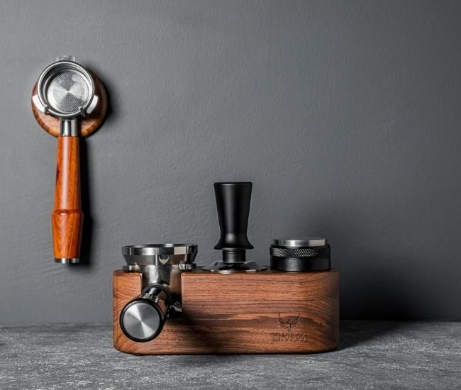 Wooden espresso tamping station holding a 58 mm portafilter, with a tamper resting in the stand